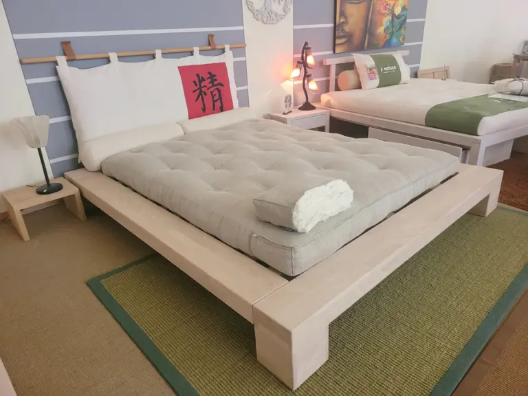 Materasso futon in canapa in posizione angolata appoggiato sulla struttura letto in legno Aiko.